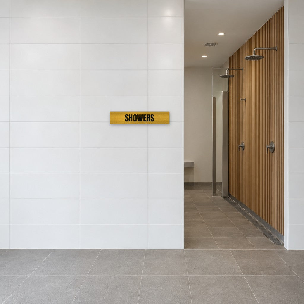 Brushed gold and black Showers sign on the tiled wall beside the showers in an Australian end-of-trip facility