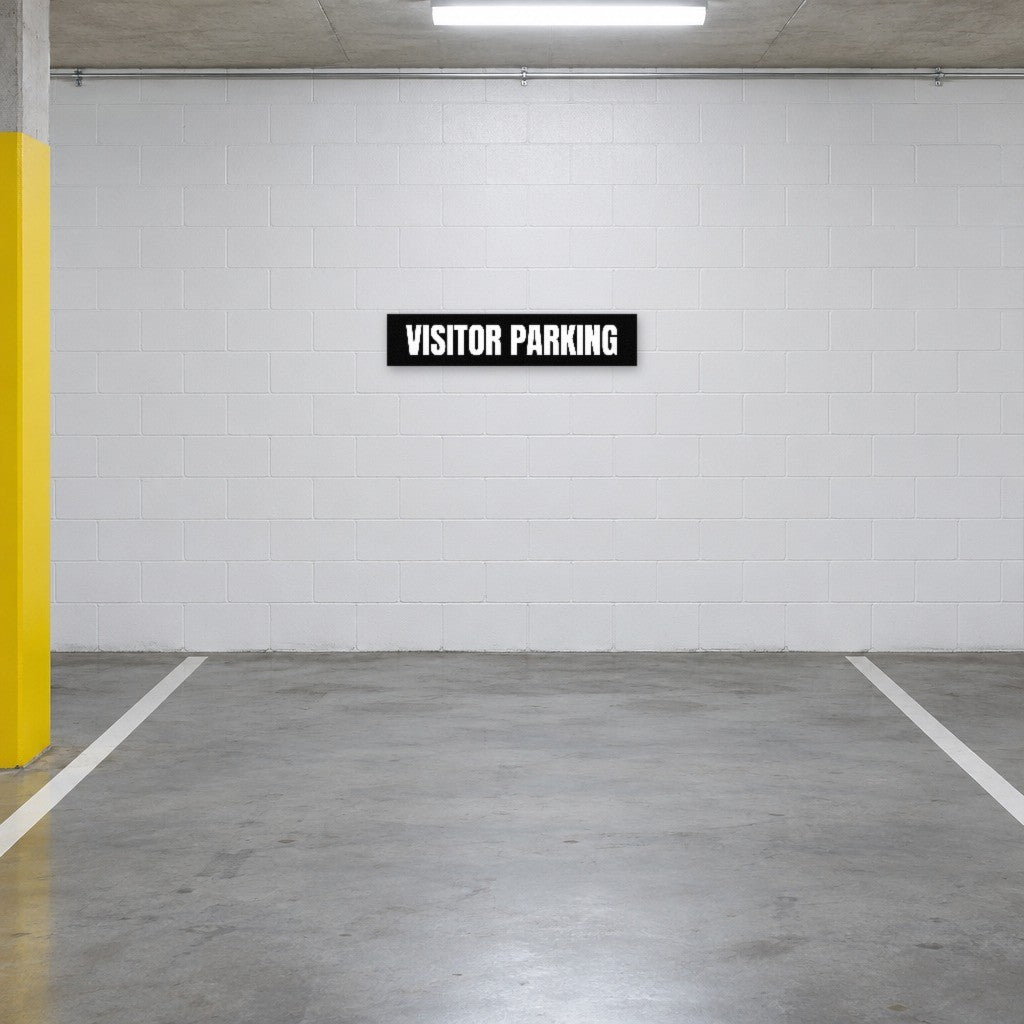 Black and white Visitor Parking sign on the wall of a visitor parking bay in an Australian basement car park