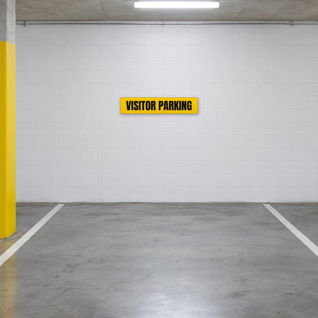 Yellow and black Visitor Parking sign on the wall of a visitor parking bay in an Australian basement car park